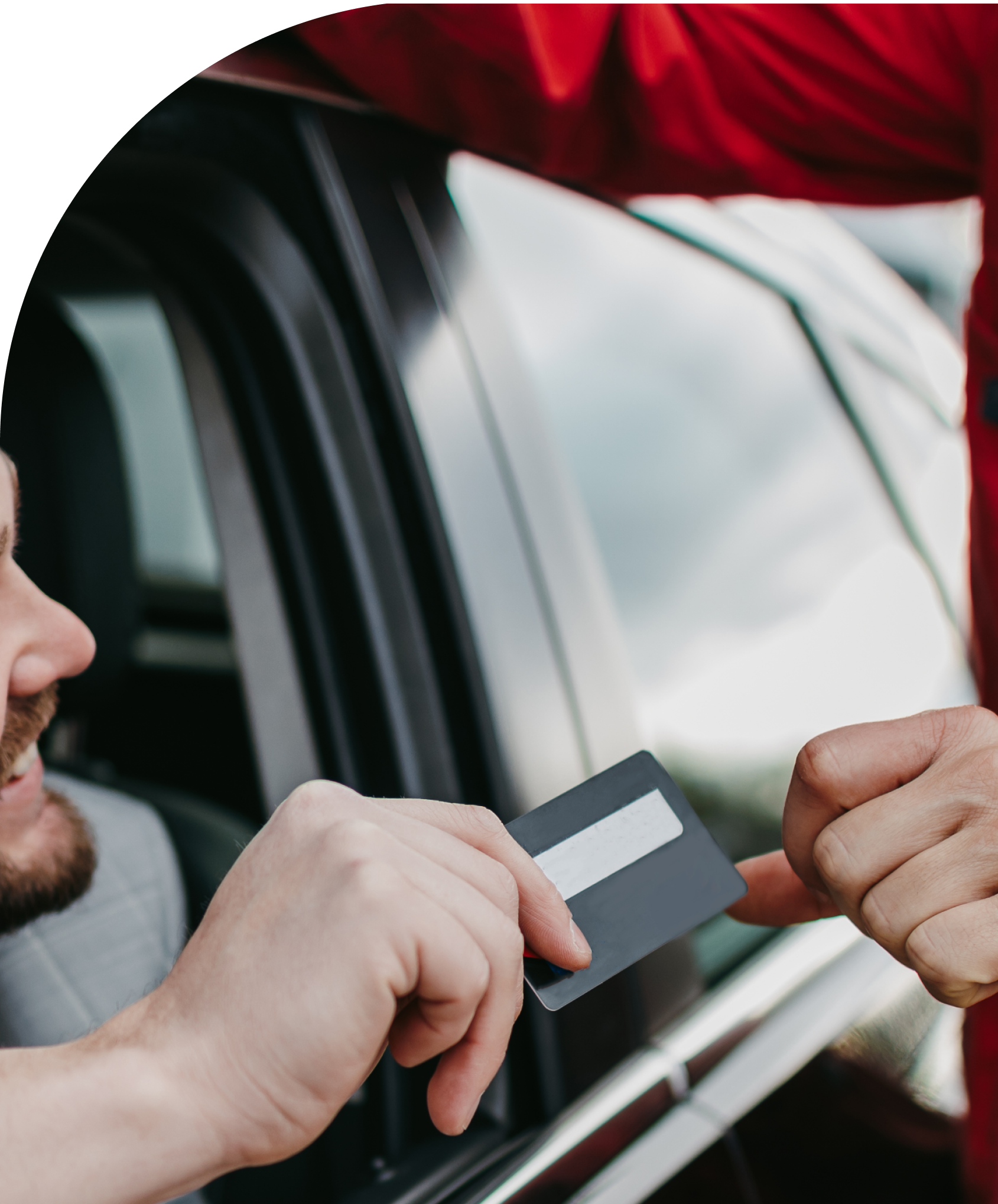 A person handing a credit card to another near a car window.